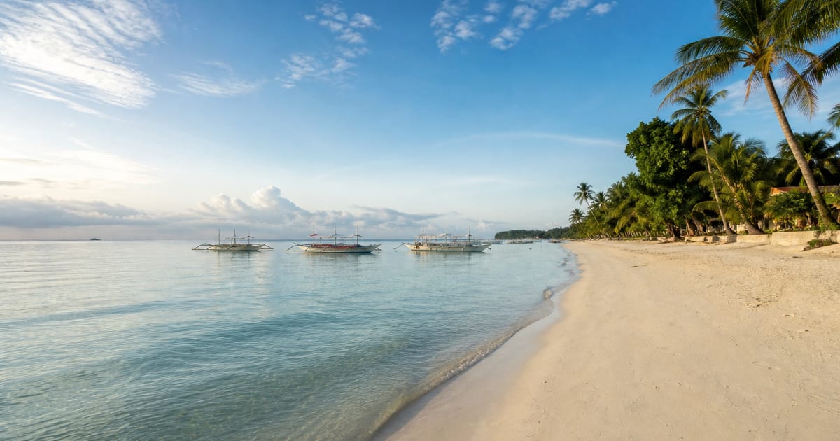Quiet early-morning shoreline and traditional outrigger boats at Alona Beach, Panglao
