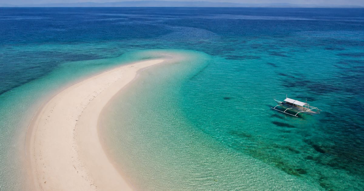 Crescent white sandbar and a small outrigger boat in clear Bohol Sea water